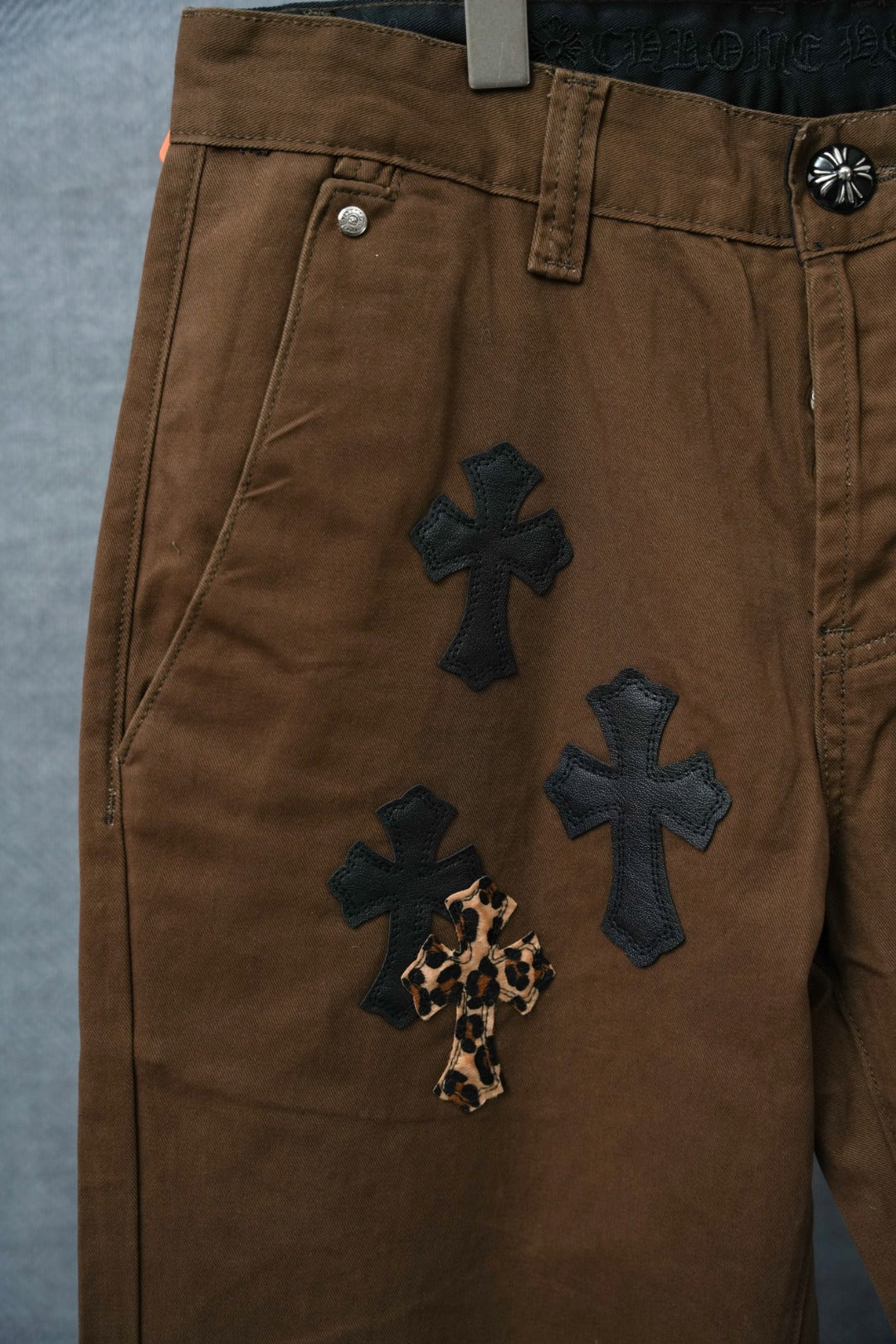 Brown pants with multiple dark cross patches and leopard-print cross accent