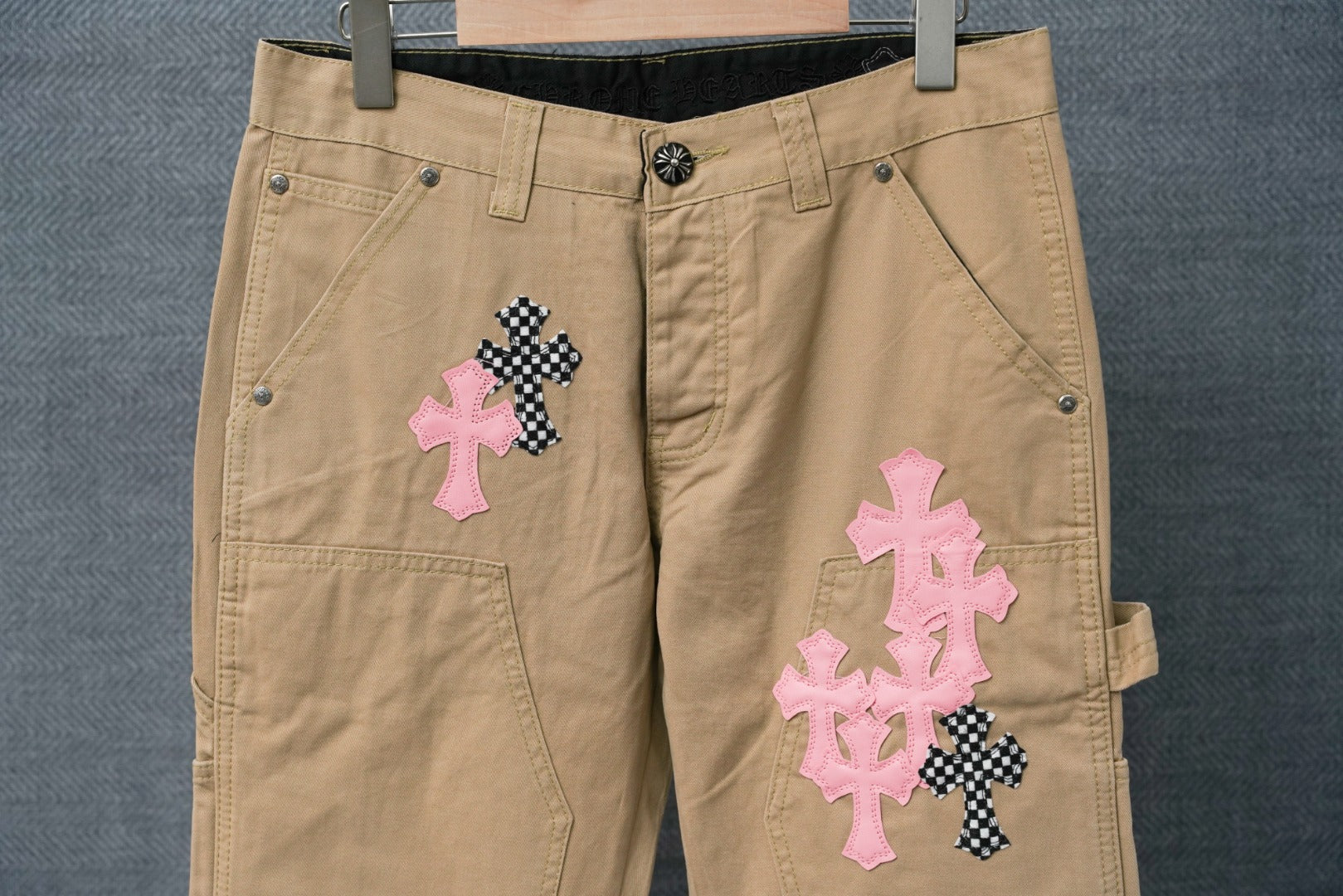 Beige cargo pants front with pink and black cross appliques and button waistband
