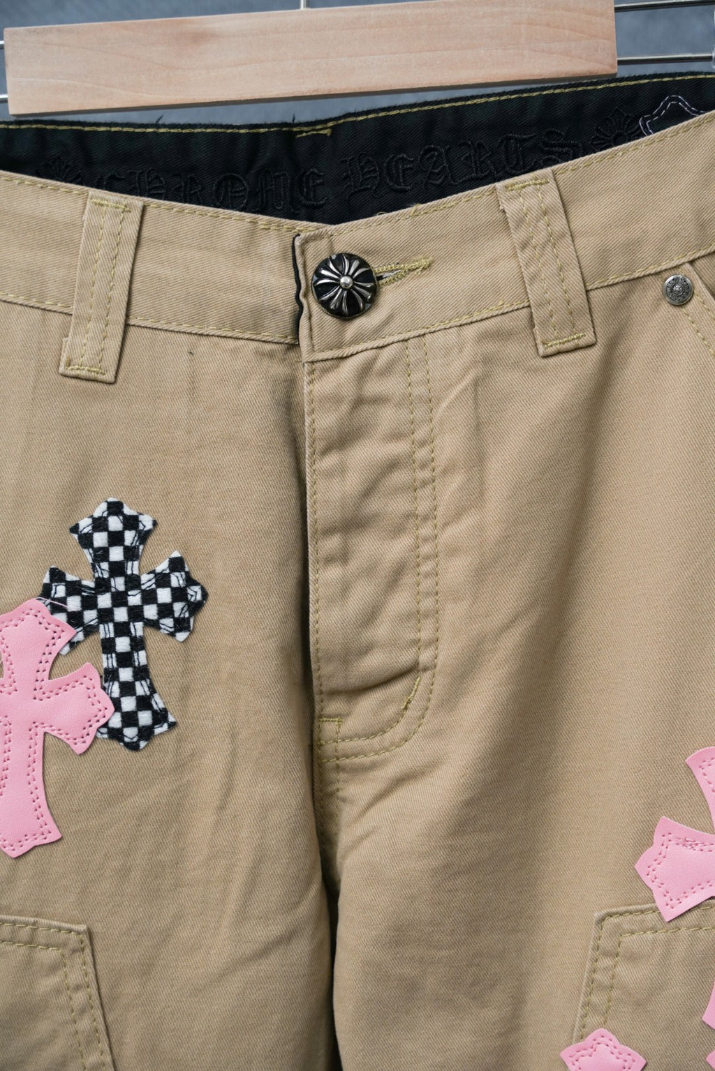 Beige pants waistband with black emblem button and pink cross patch