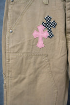 Beige cargo-style pants with pink and black check cross patches on the front leg