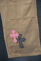 Beige pants with pink and black checkered cross appliques on cargo pocket