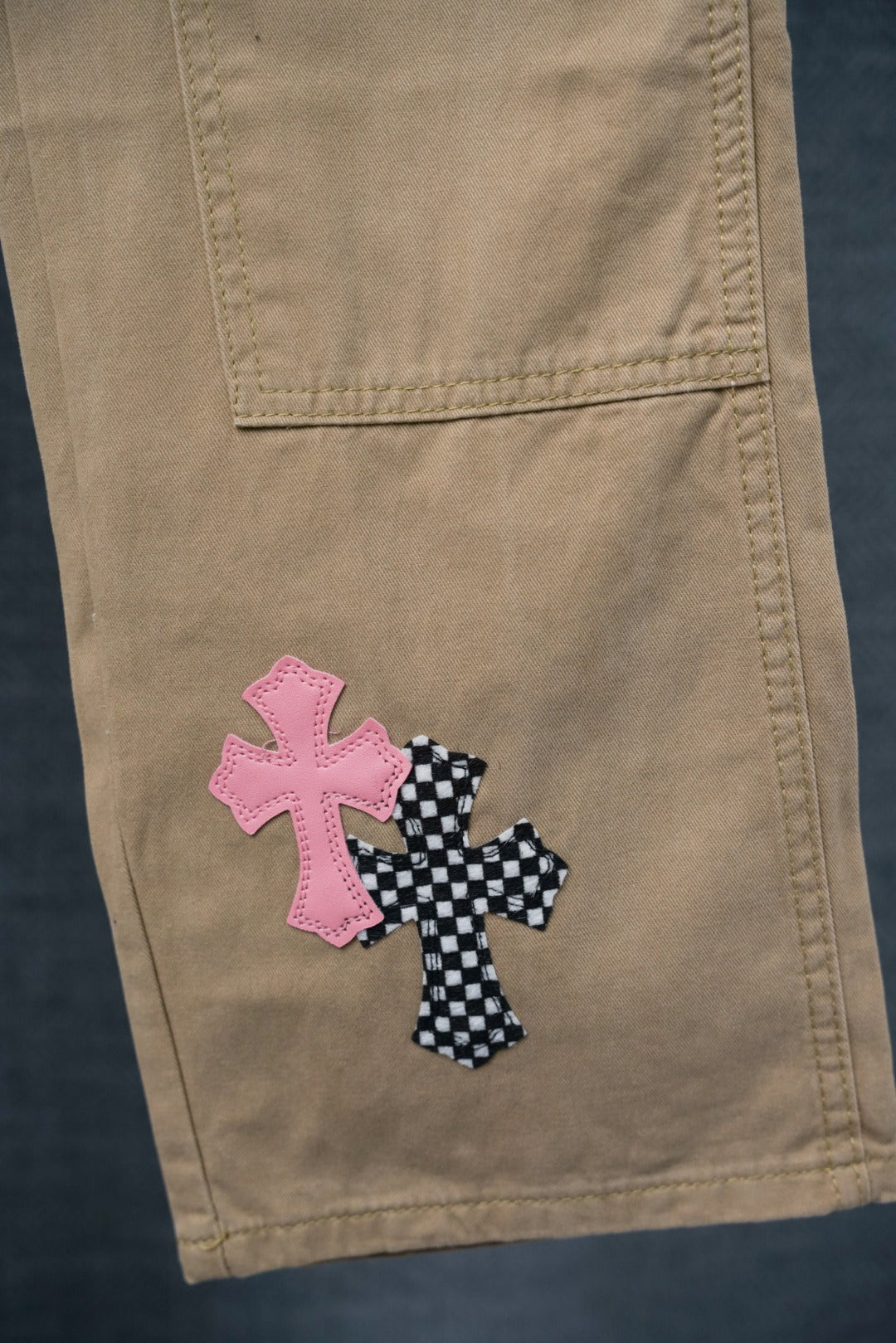 Beige pants with pink and black checkered cross appliques on cargo pocket