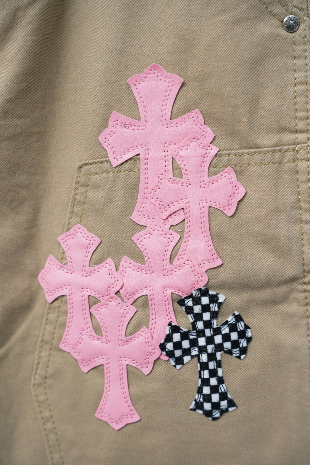 Close-up of pink cross and black check cross appliques on tan fabric