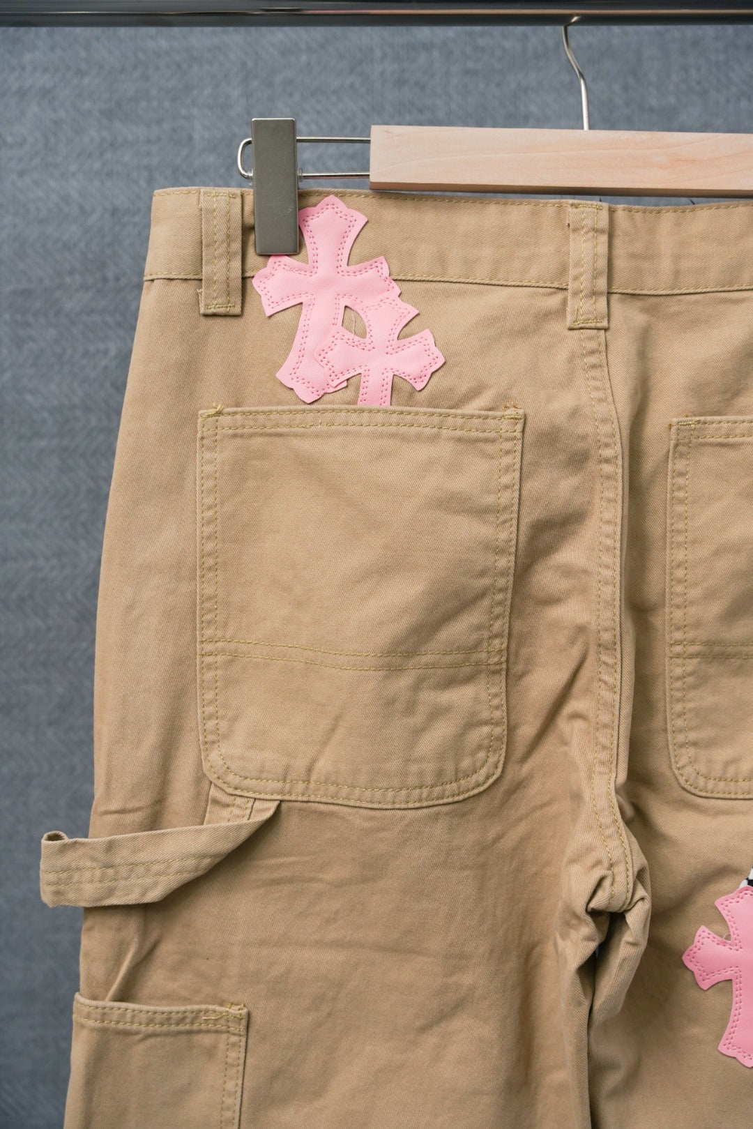 Beige cargo pants with large pink cross patch on pocket area