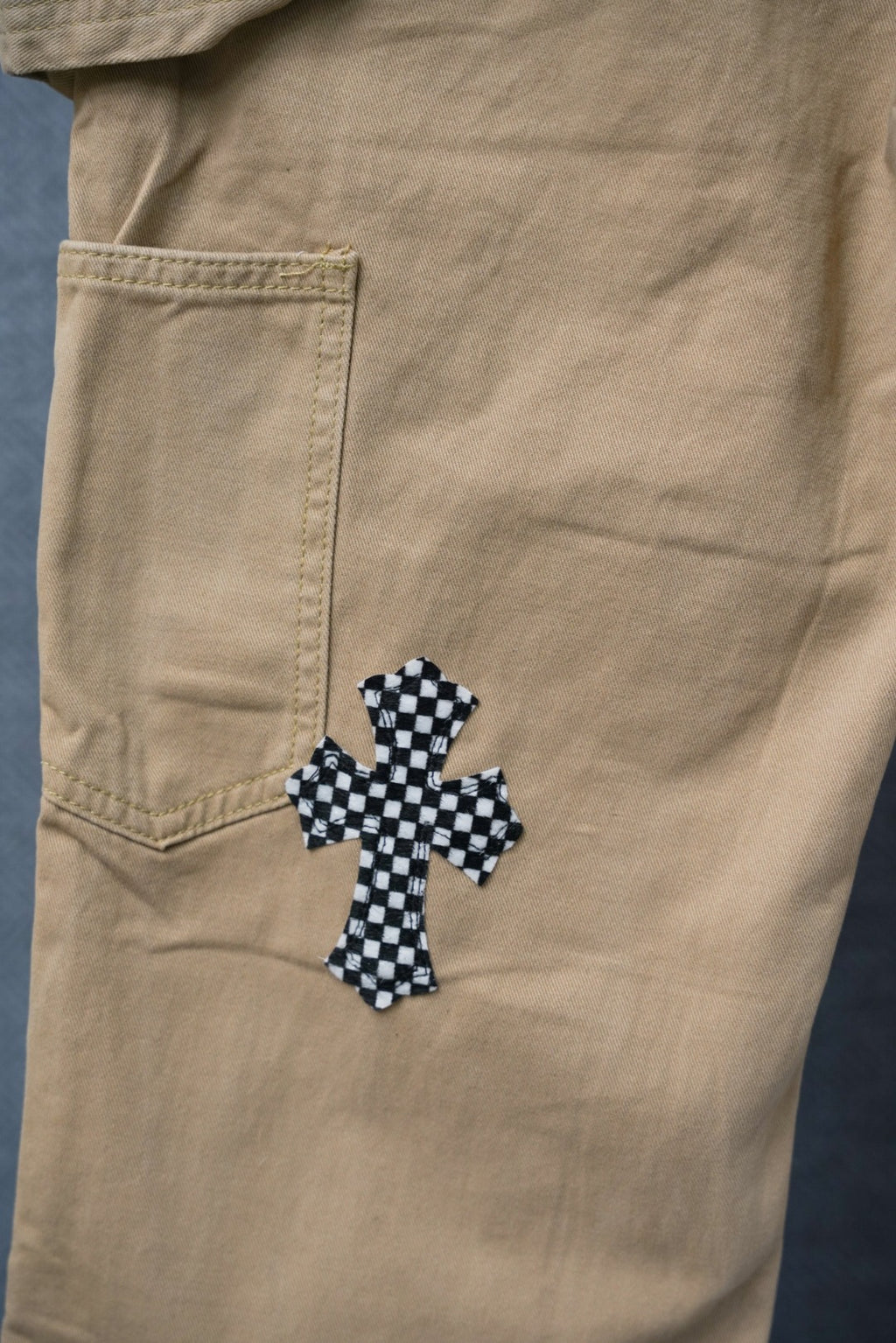 Beige cargo pants with black-and-white check cross applique on the front leg