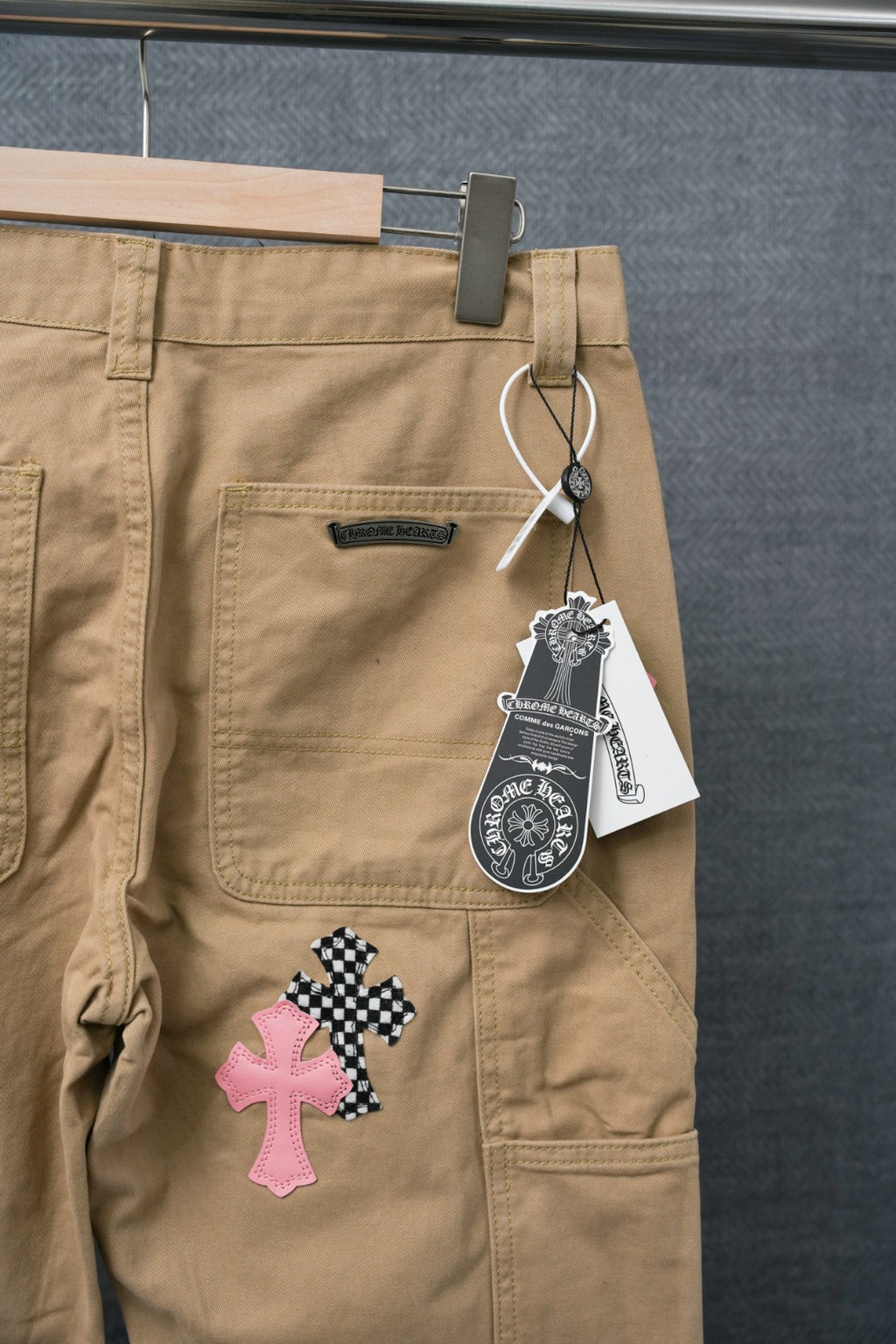 Beige cargo pants with front patch pockets and hanging price tag; check and pink cross appliques