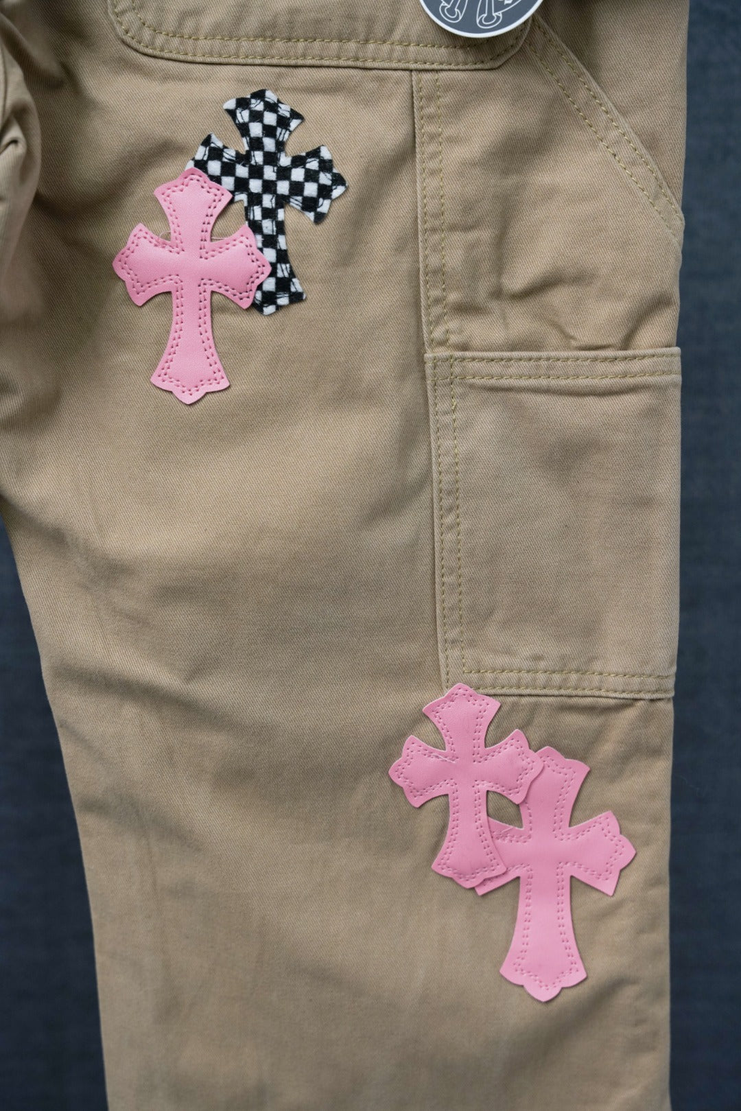 Beige cargo pants with pink and black check cross patches on the front