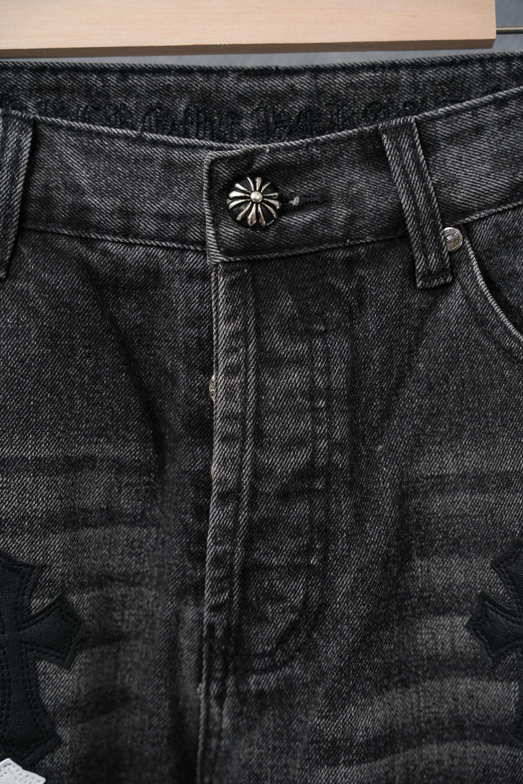 Black denim waistband with small starburst pin and button, close-up