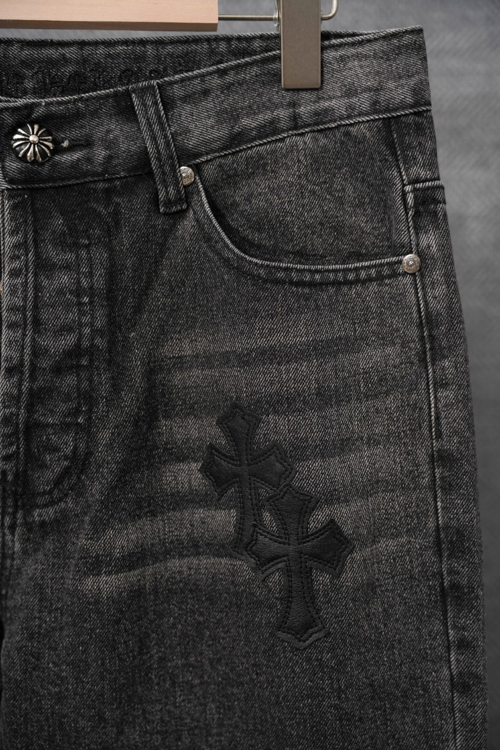 Black denim pants with coin pocket and large dark cross applique, close-up