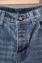 Blue denim Chrome pants with button-and-emblem detail on waistband.