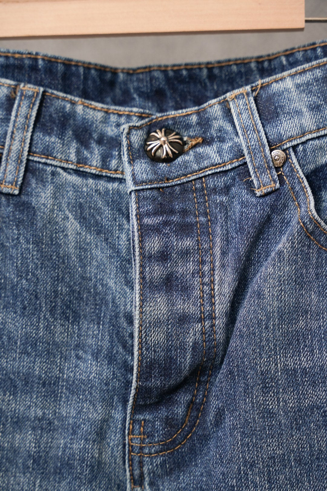 Blue denim Chrome pants with button-and-emblem detail on waistband.