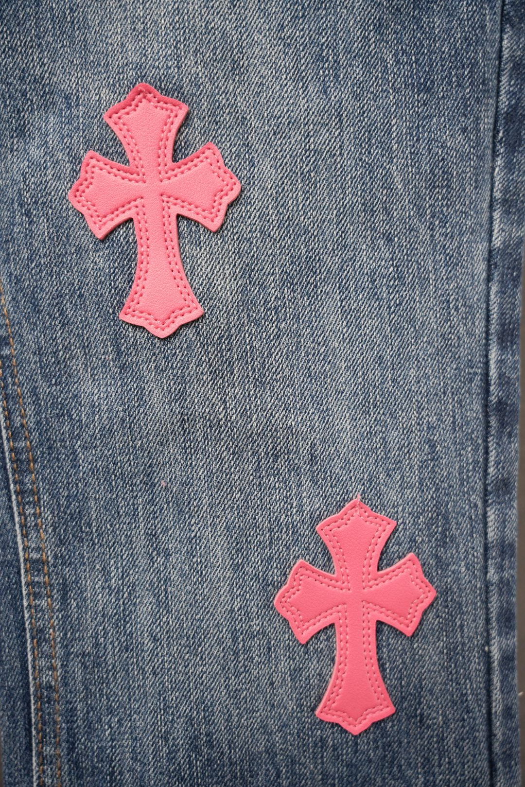 Blue denim Chrome pants close-up of pink cross patches near pocket.