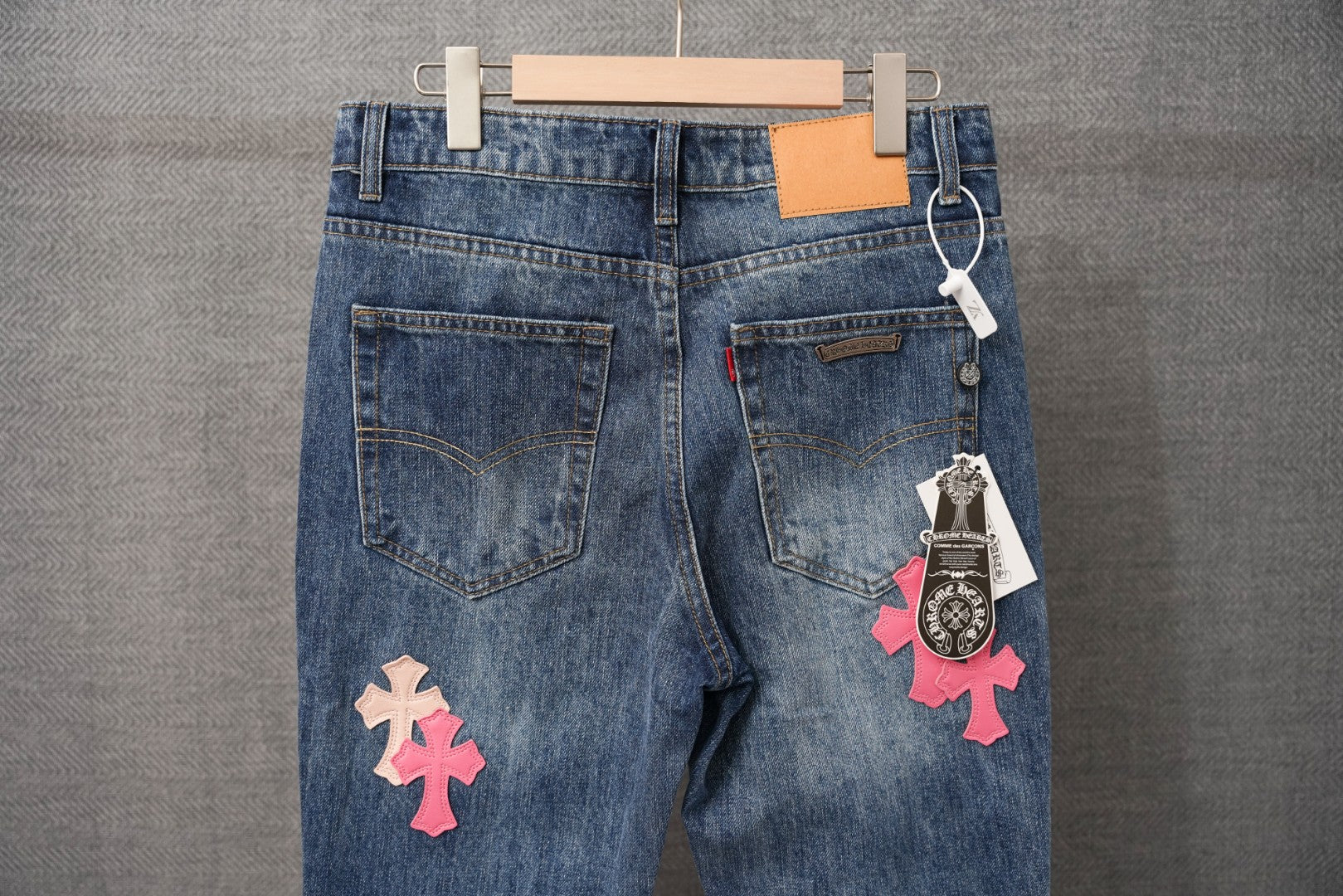 Blue denim pants with front pockets and pink/beige cross patches; hang tag
