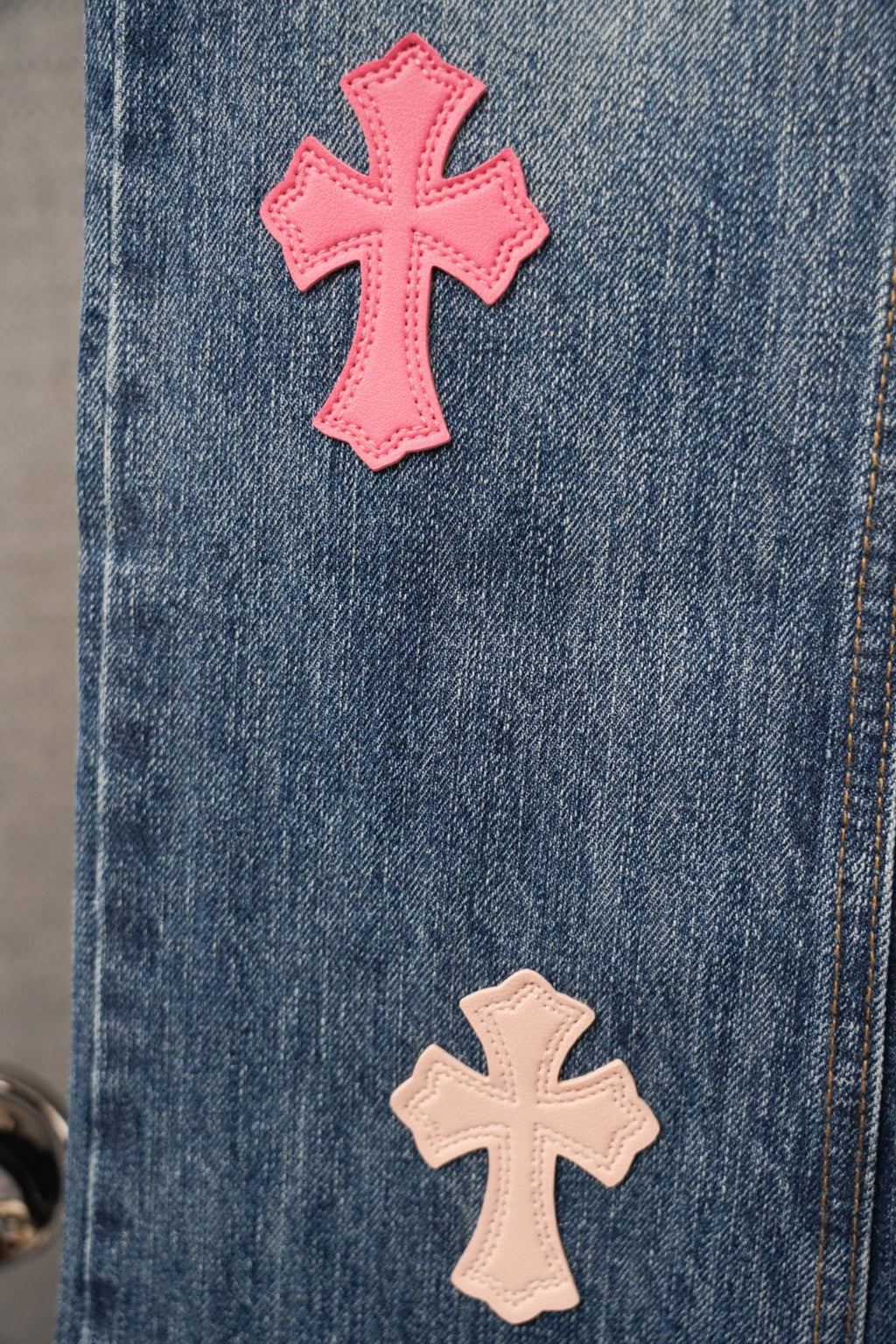 Blue denim pants with pink and beige cross patches on front pocket area