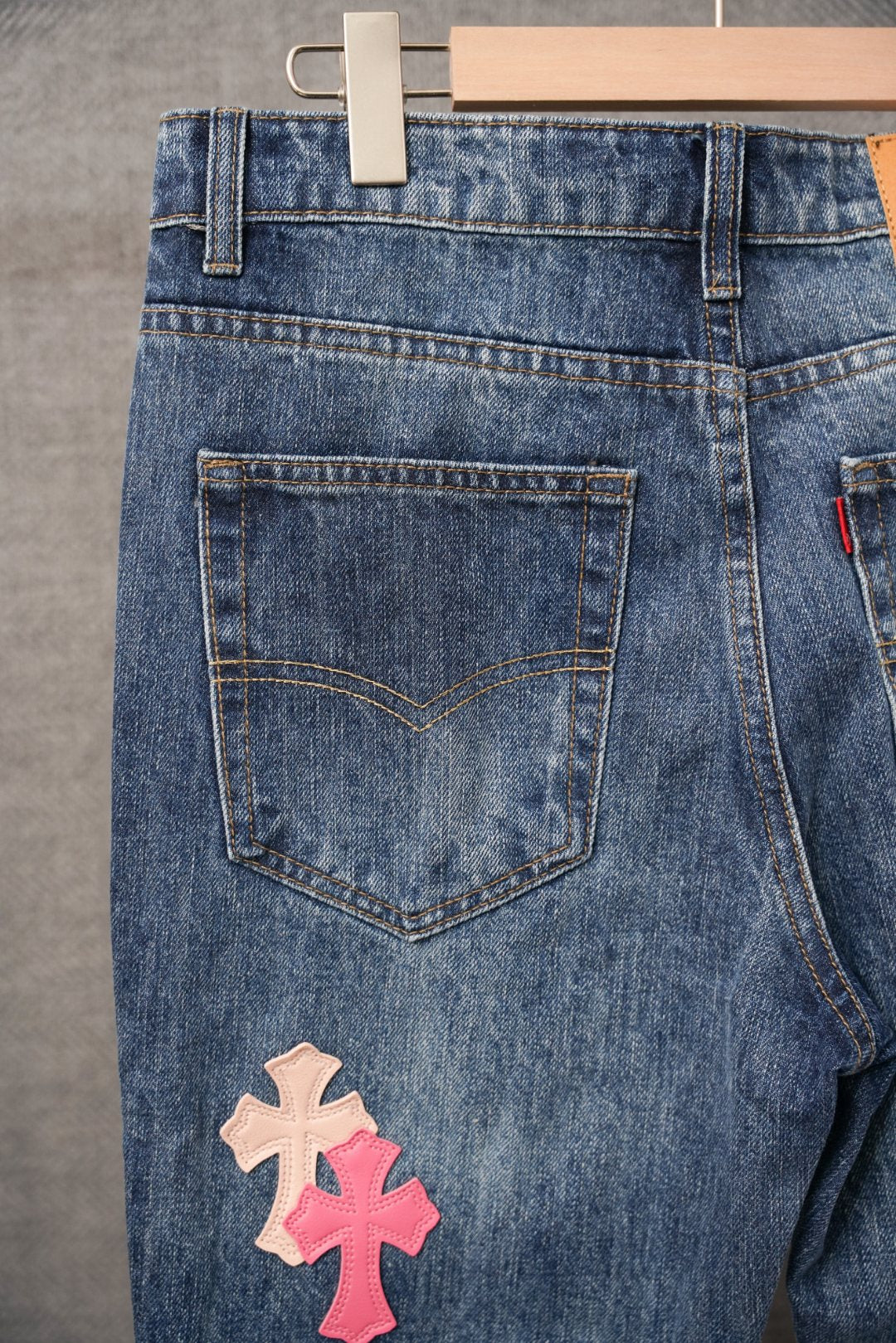 Blue denim jeans with front pockets and two pink cross patches near hem