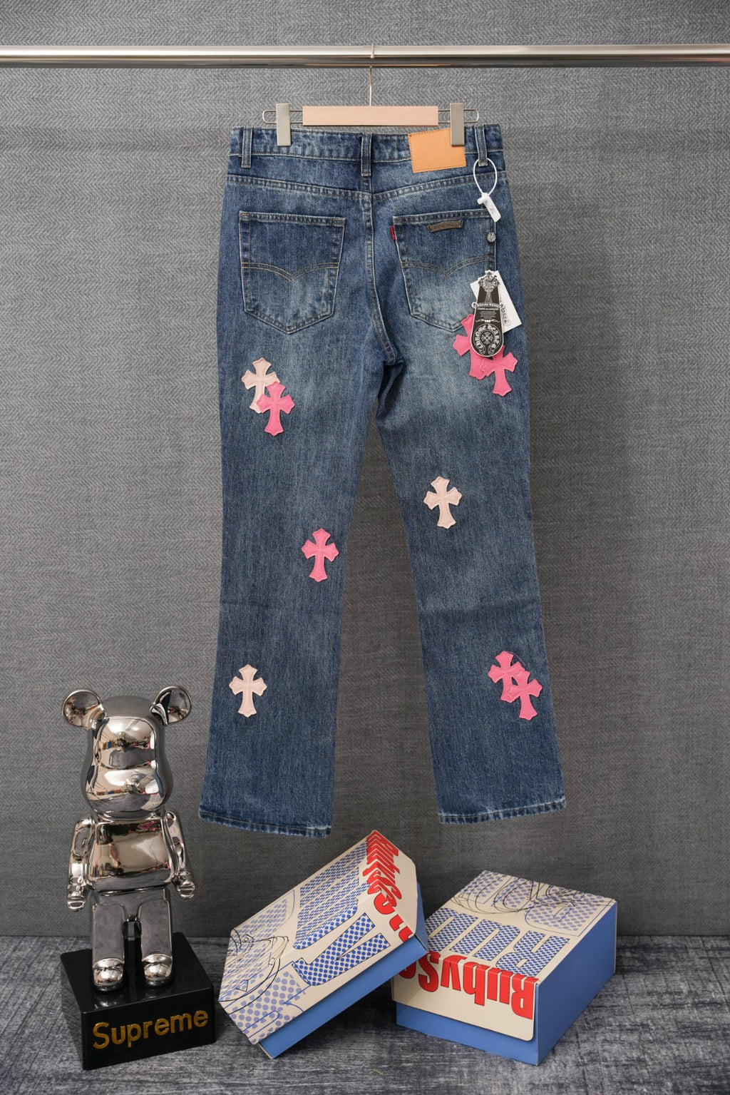 Blue denim Chrome pants with scattered pink and peach cross patches, side view.