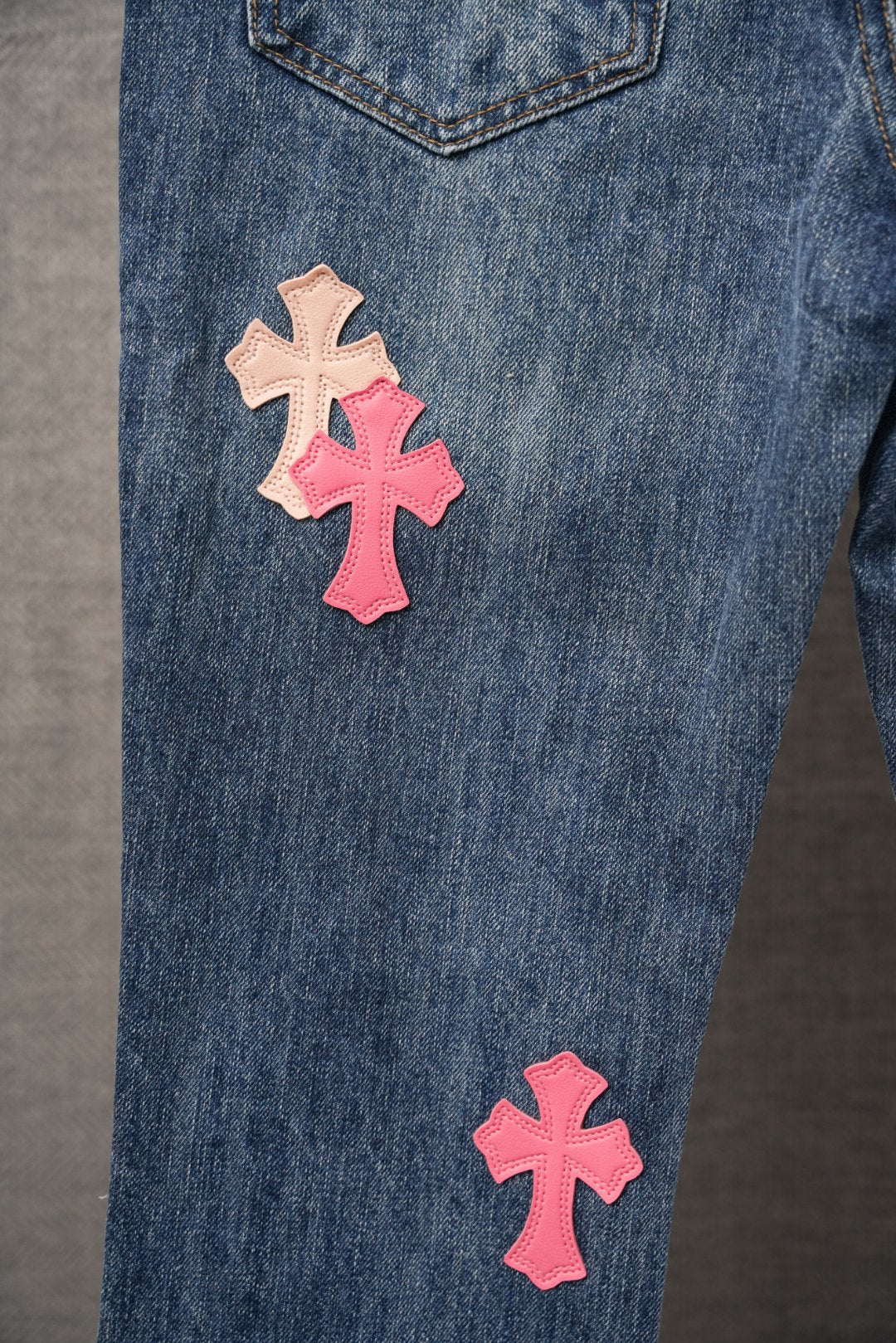 Blue denim jeans with pink and beige cross patches on upper and lower legs