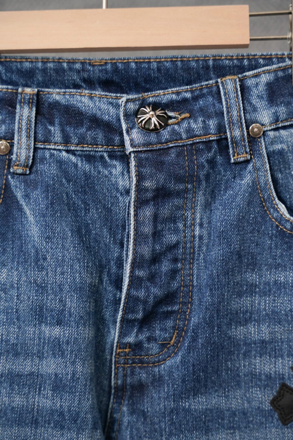 Blue denim jeans waistband with button fly and cross patch detail.