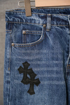 Blue denim pants with black cross applique on front near hip.