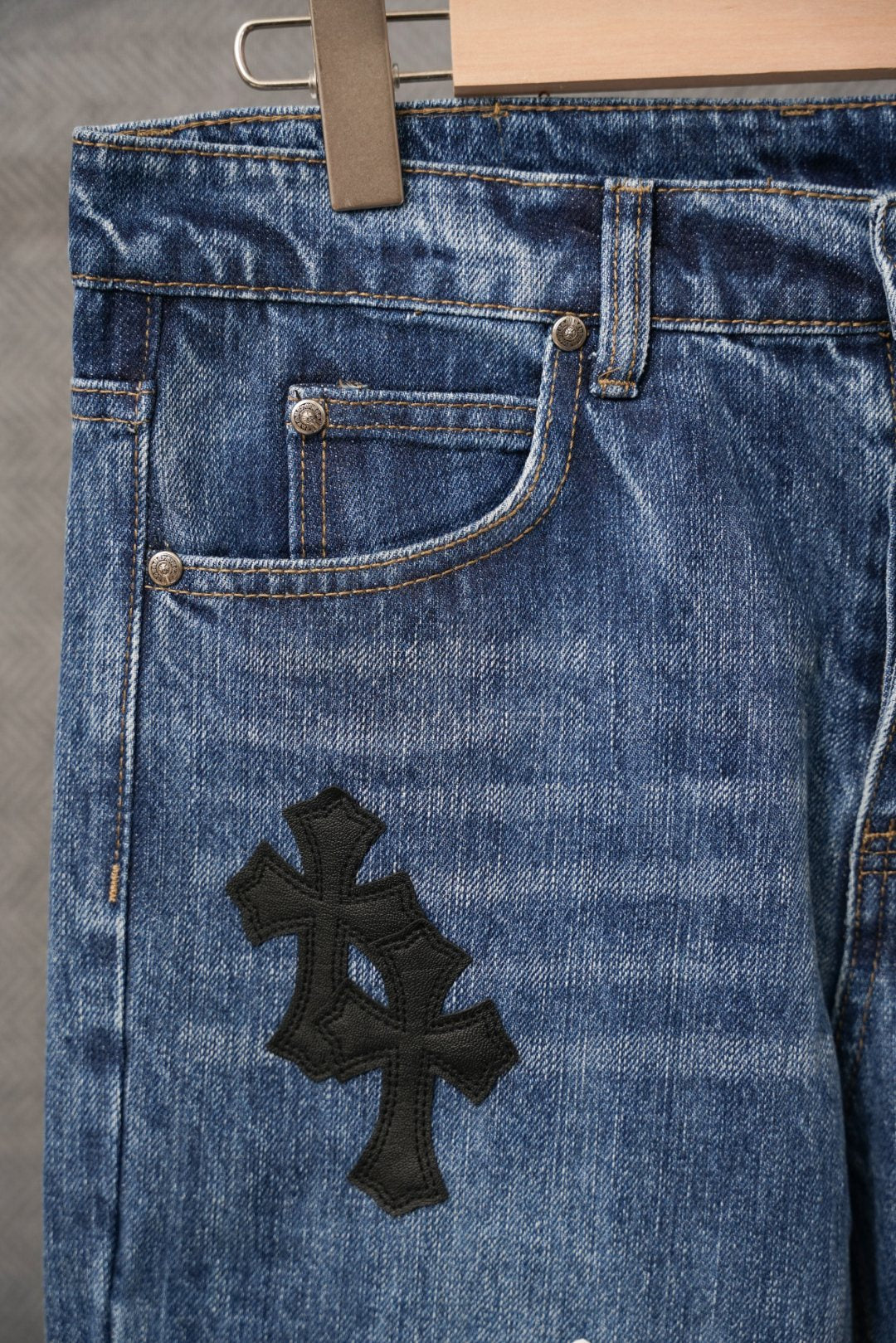 Blue denim pants close-up of front pocket with black cross patch