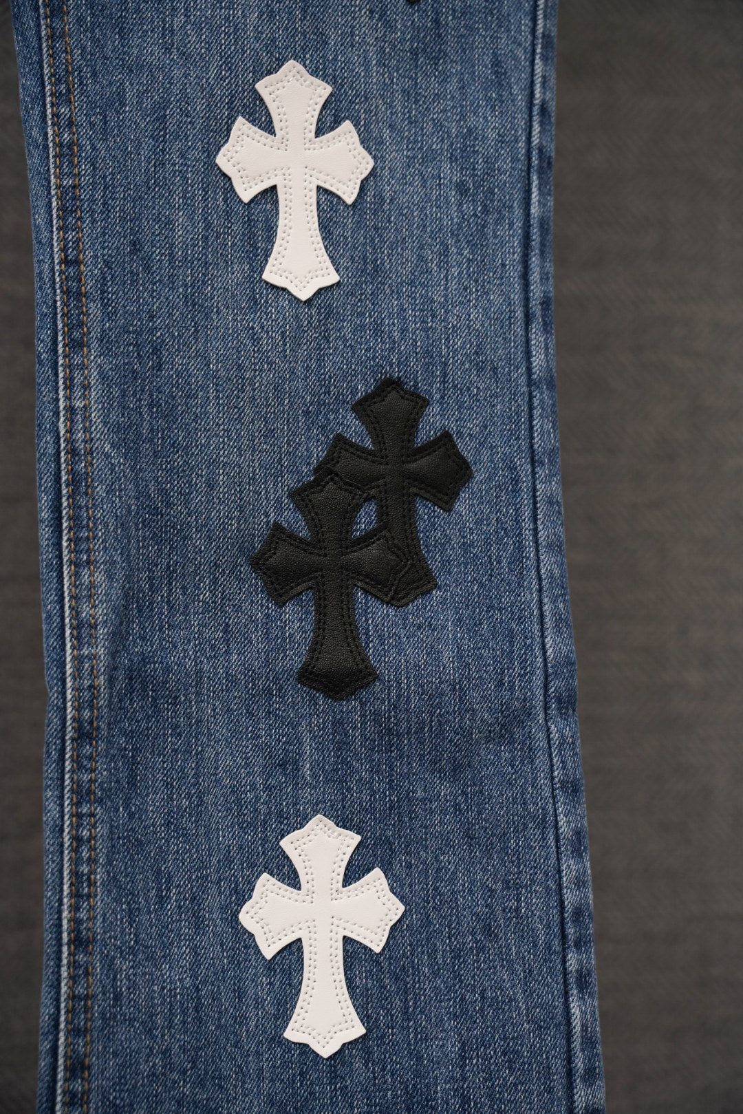 Blue denim pants with white and black cross patches along front seam.