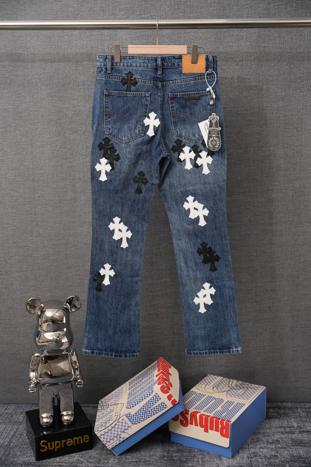Blue denim pants with scattered dark and white cross appliques on front.
