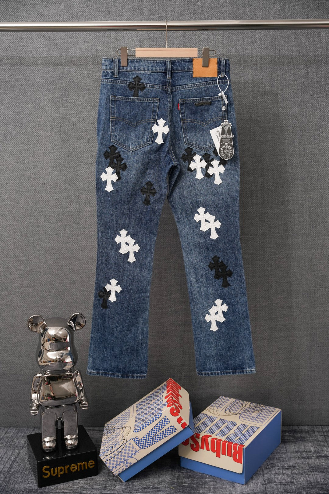 Blue denim pants with scattered dark and white cross appliques on front.