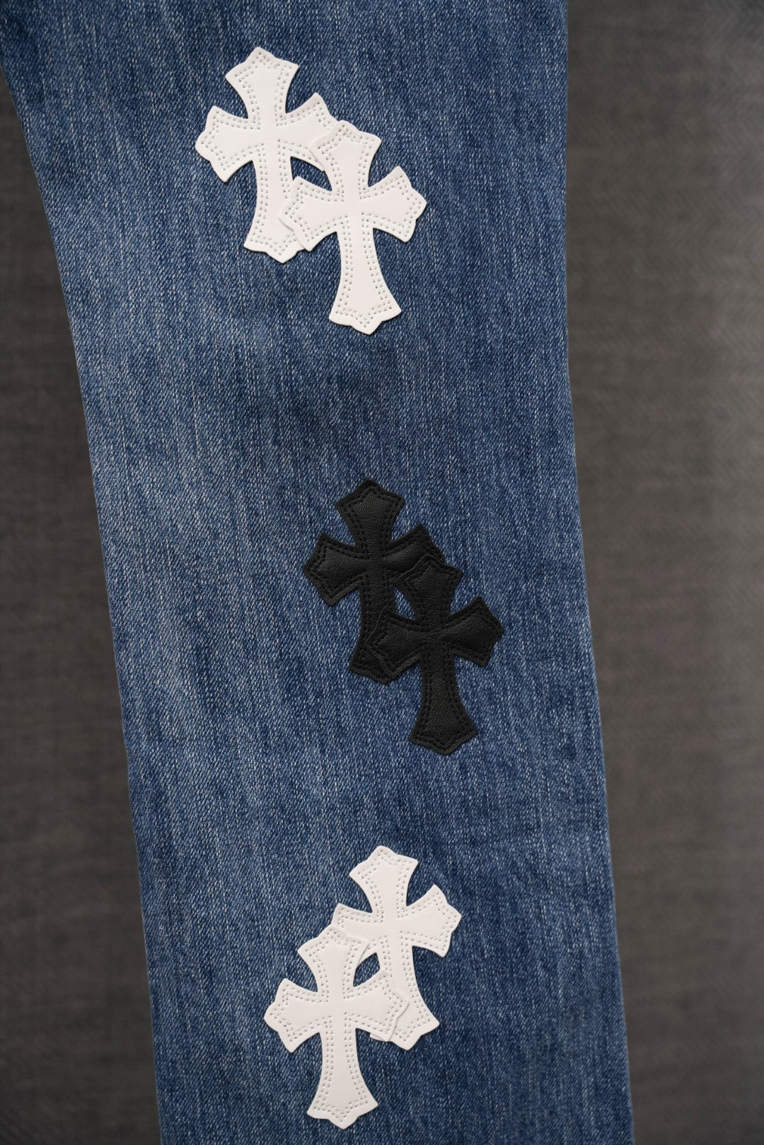 Blue denim pants with cross appliques scattered down the leg