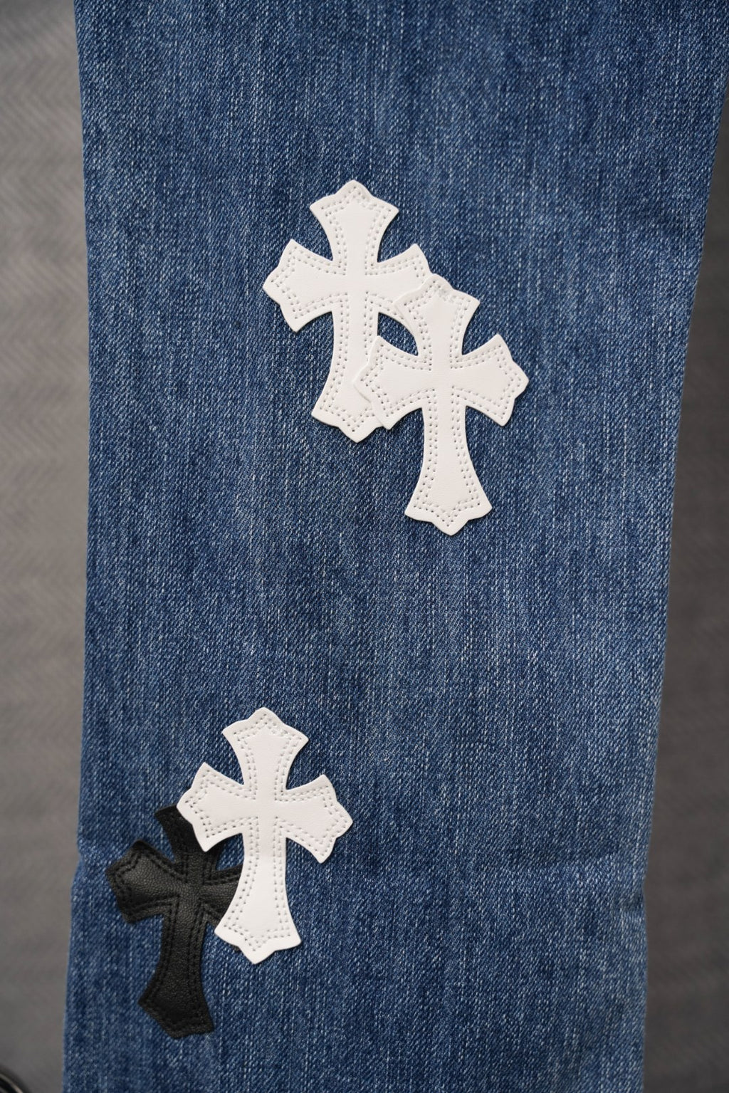Blue denim pants with white and black cross patches on leg