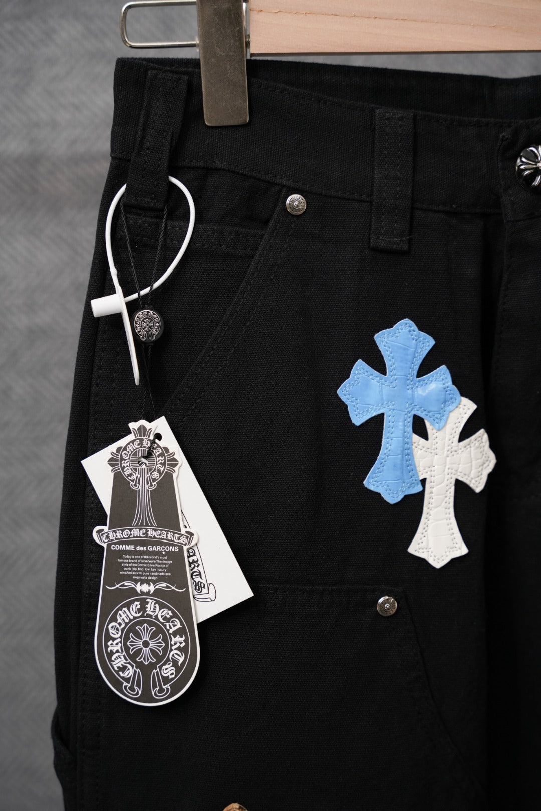 Black pants close-up of waistband and front pocket with hanging cross tag