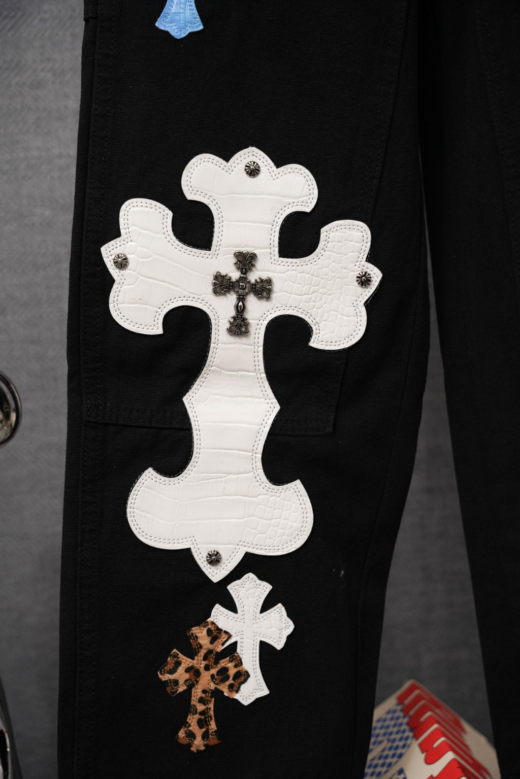 Black pants close-up of large white cross applique with small leopard print cross patch