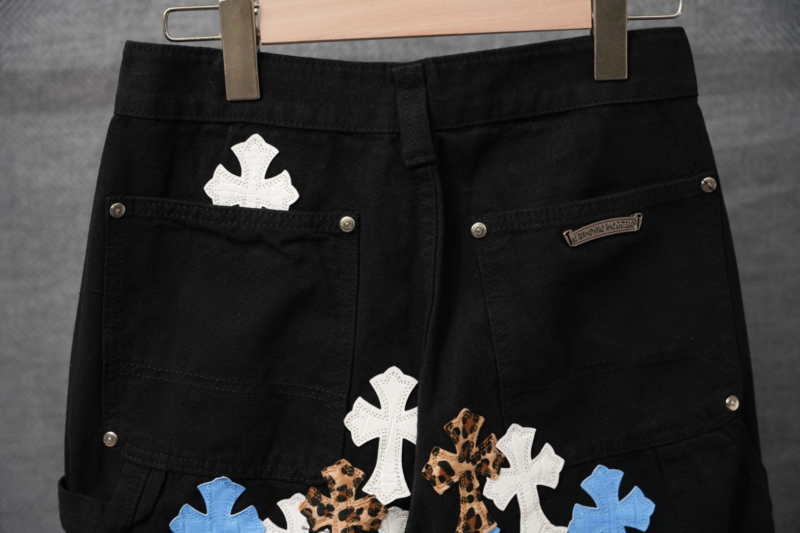 Black pants close-up of back pockets with white, blue, and leopard cross appliques