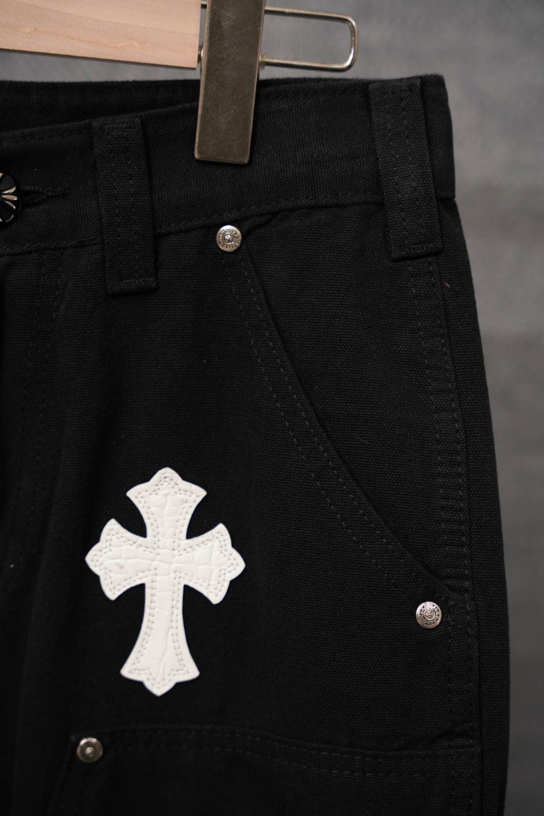 Black pants front close-up with white cross patch and side pocket metal button.