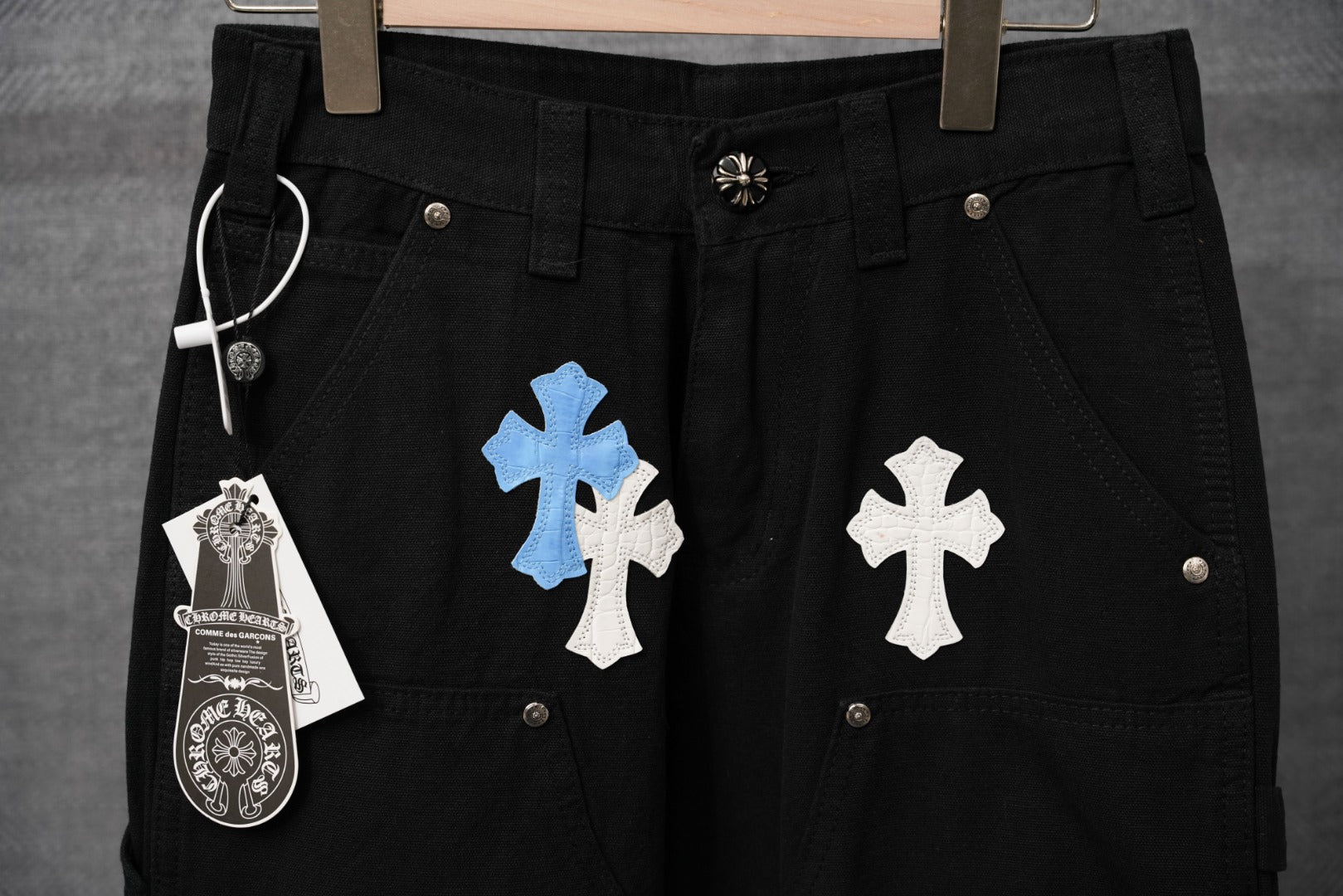 Black pants close-up showing blue and white cross patches and pocket button hardware.