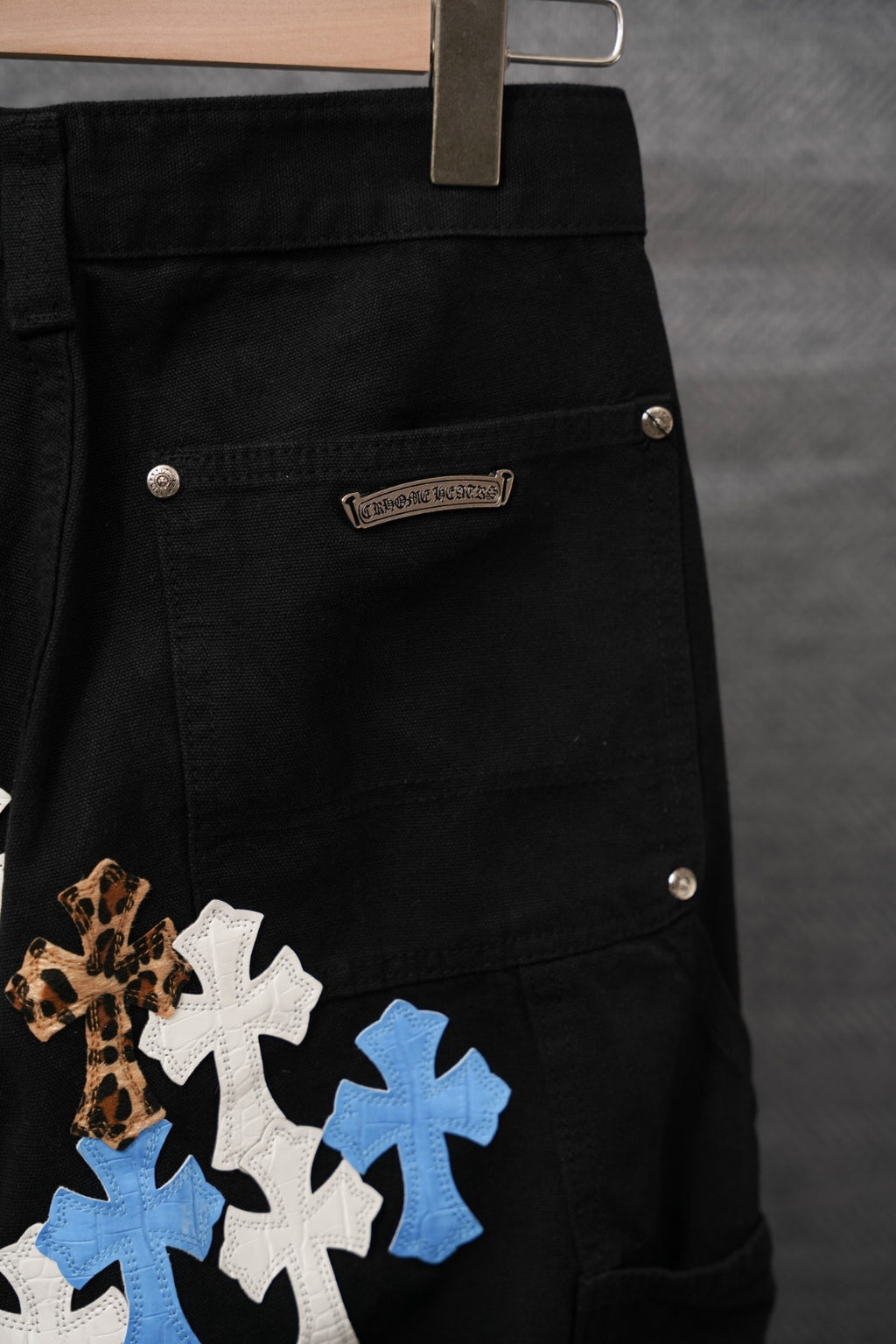Chrome pants, black denim with cross patches and metal button close-up