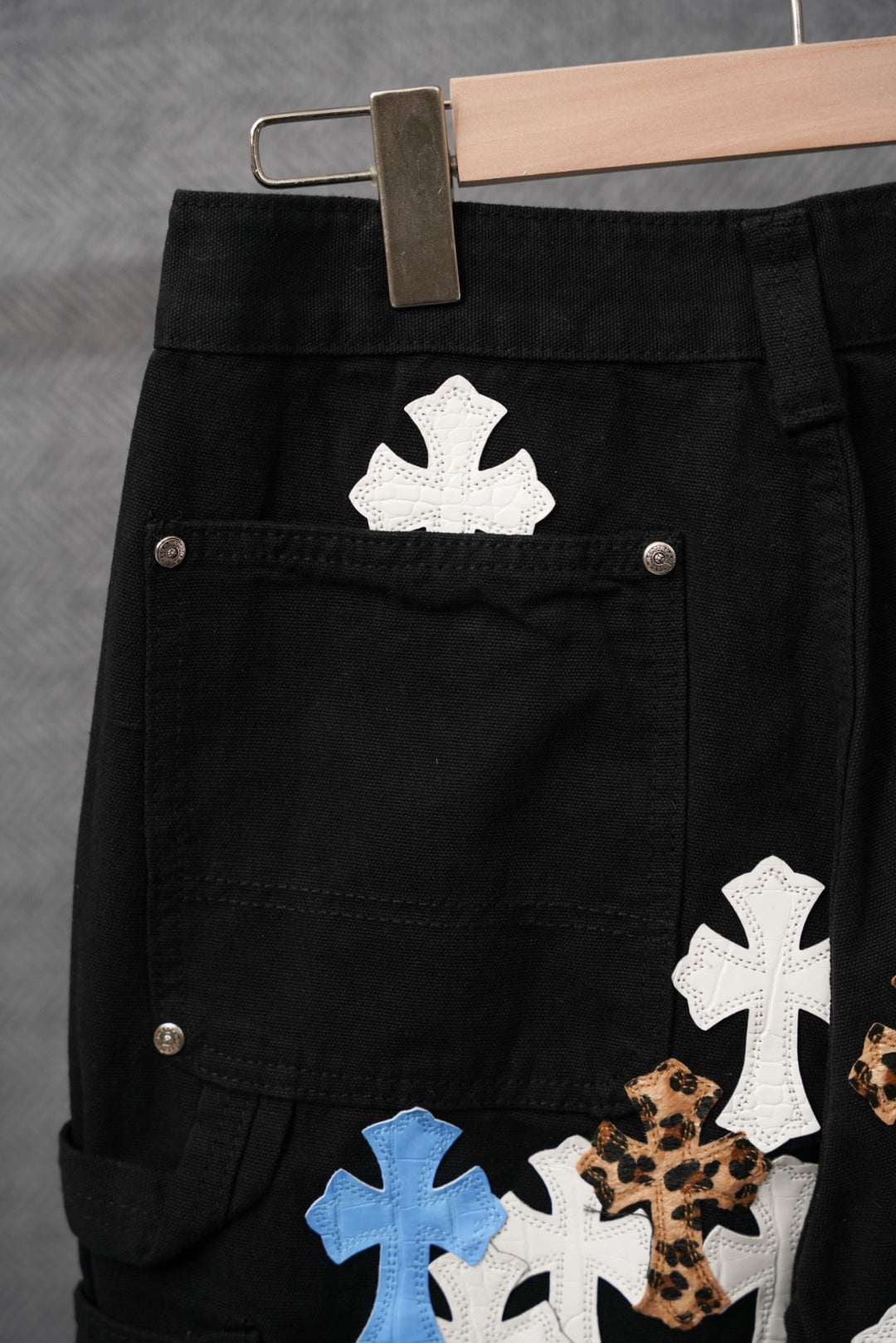 Black pants close-up of front pockets with white and blue cross applique patches