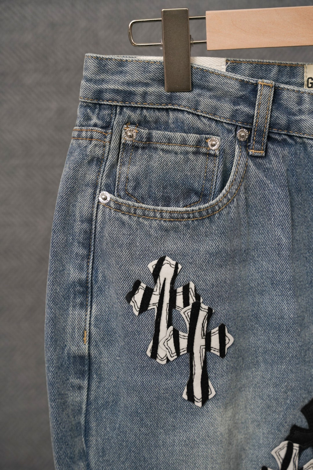 Light-wash denim jeans with front buttoned pocket and black cross appliqué