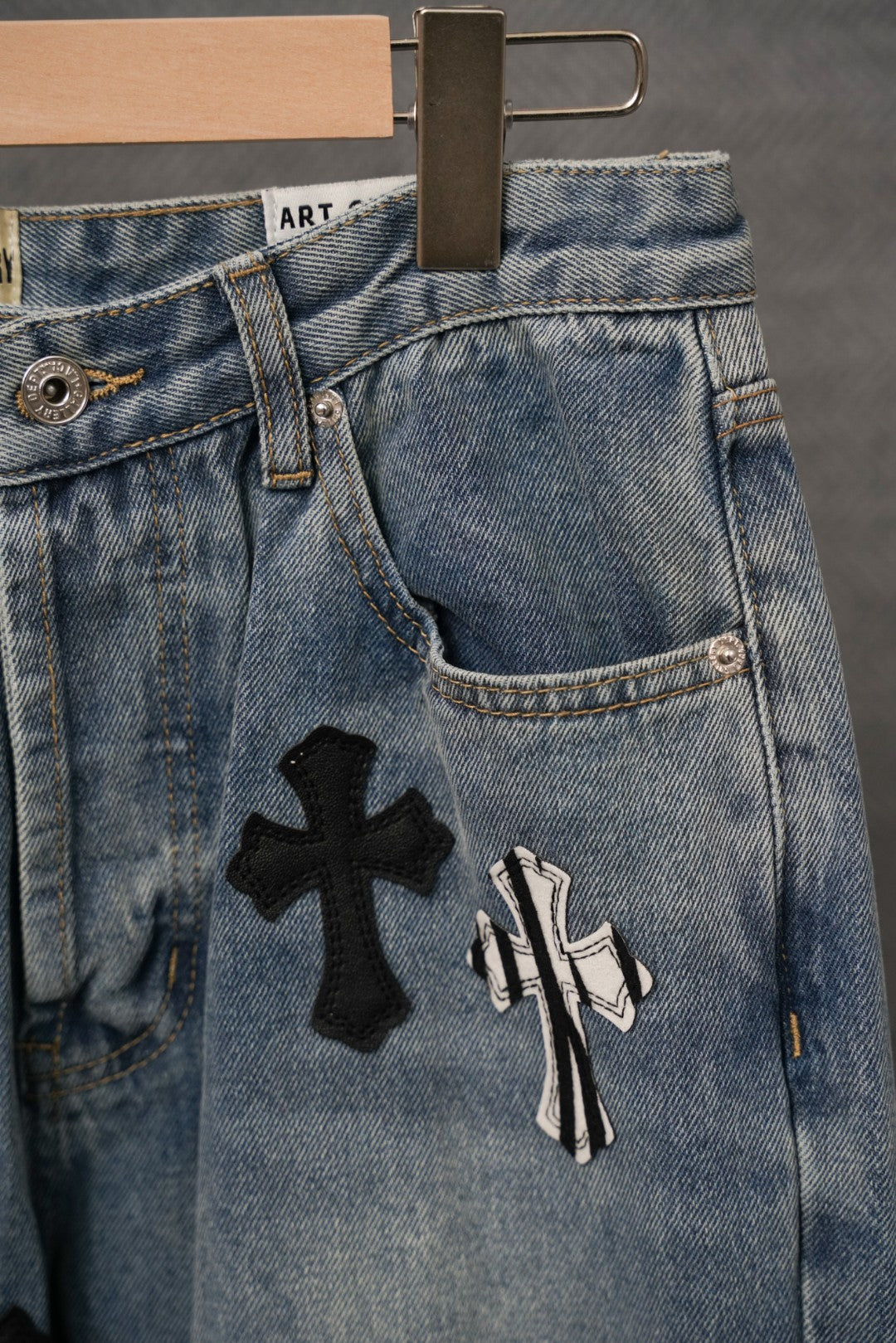 Light-wash denim jeans with belt loops, stitched fly, and black cross patch
