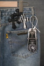 Light blue denim pants with black cross and striped patch graphics; hanging charm tag