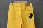 Chrome pants in bright yellow with patterned textural stitching and a hanging tag at the waistband.