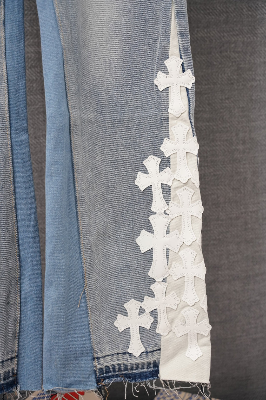 Light-wash denim pant leg with vertical stack of white cross appliques