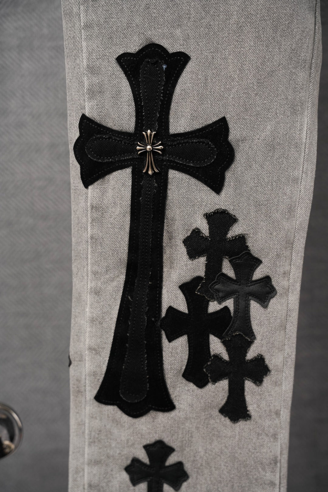 Light gray denim pants with tall black cross graphic and smaller cross patch.