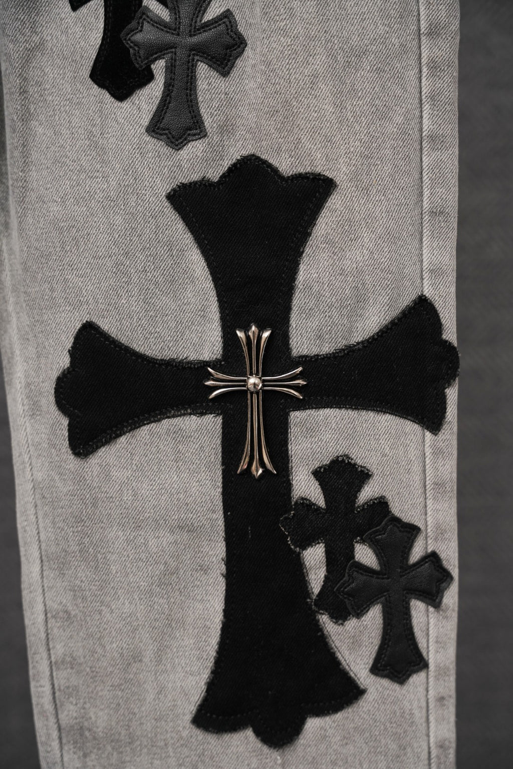 Light gray denim pants with large black cross patch and smaller cross graphics.