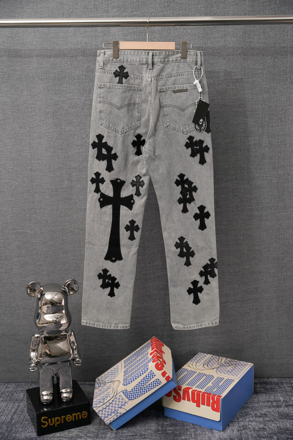 Light-wash denim pants with black cross appliques, back pockets and waistband