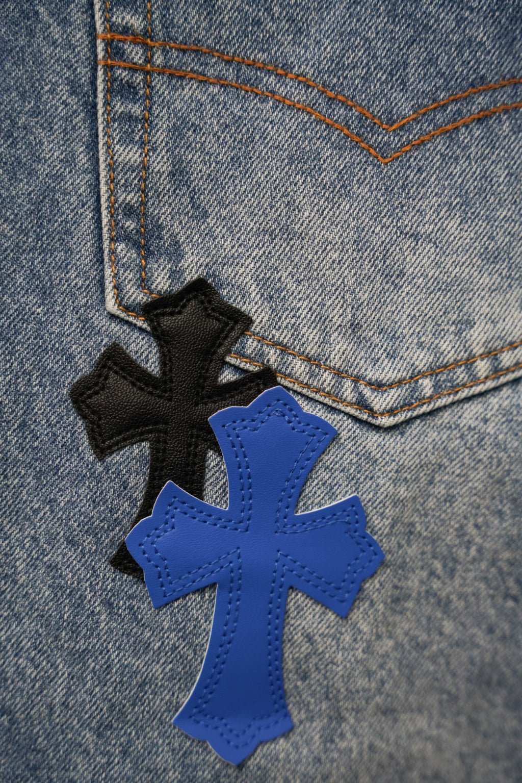 Embroidered cross patch detail on light blue denim; black, blue, and stitched accents