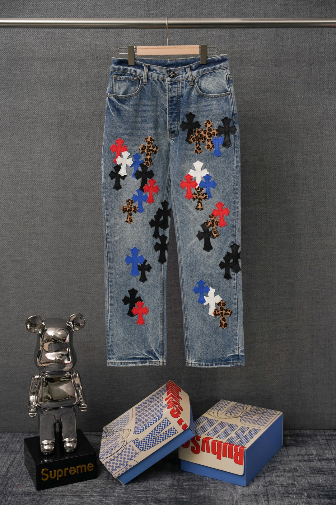 Light blue denim pants with multicolor embroidered cross patches on the front