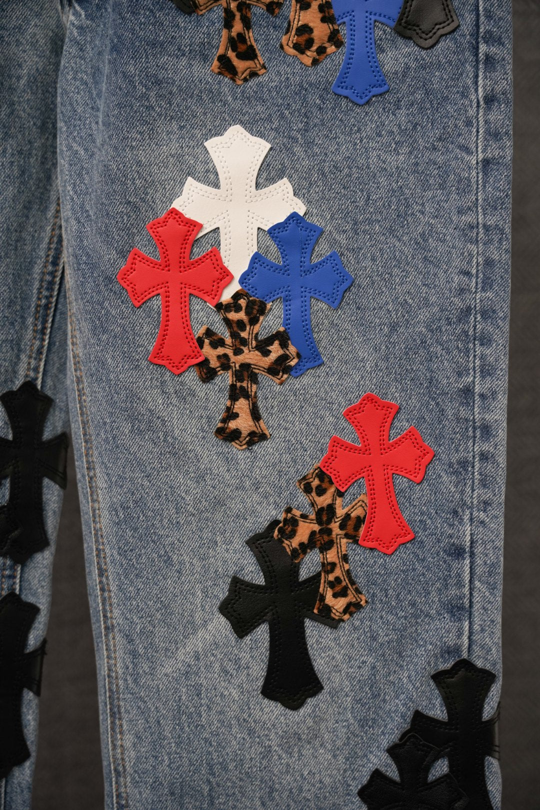 Close-up of embroidered cross patches on light blue denim, including leopard-style crosses