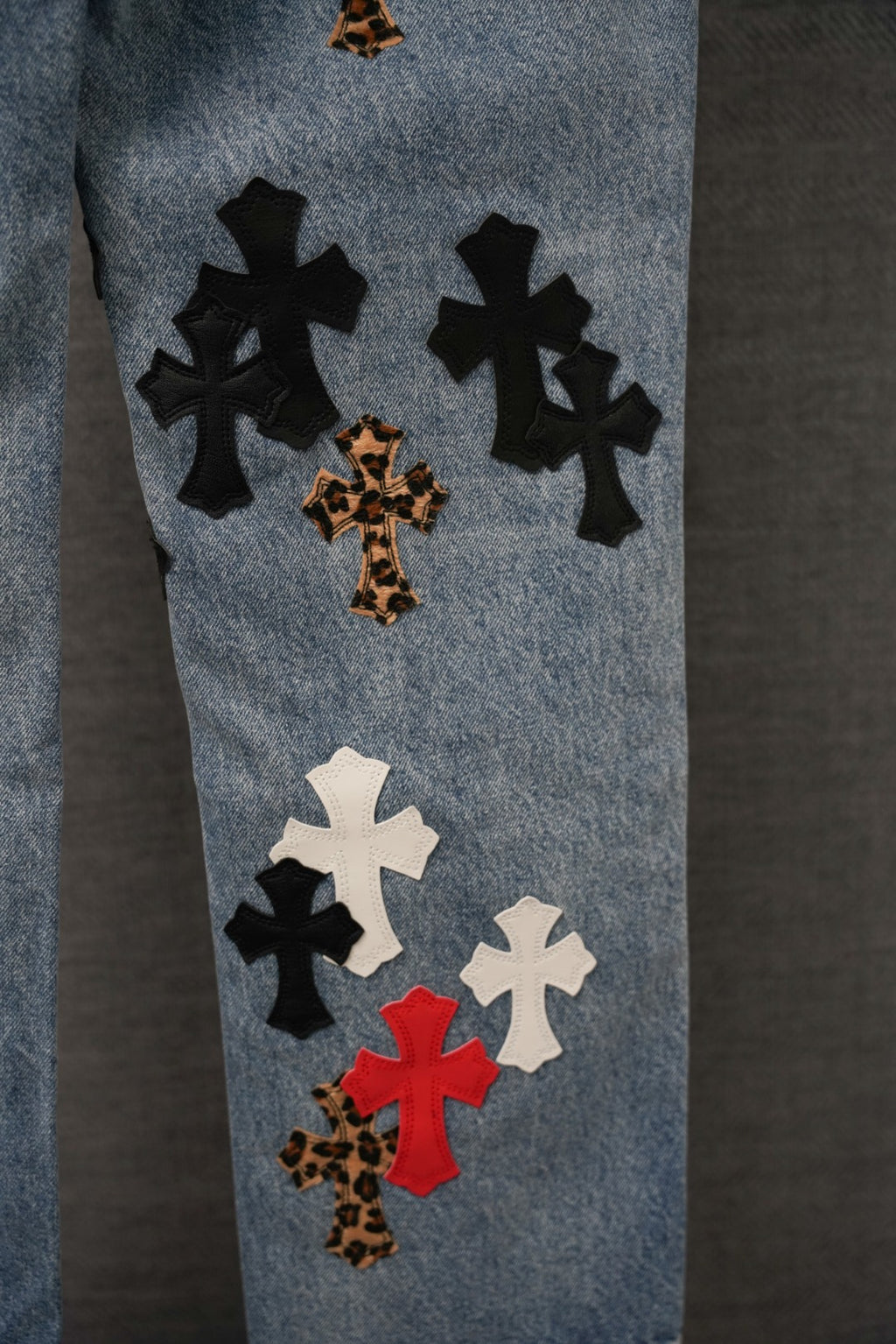 Blue denim pants with cross patches in black, white, red, and leopard print