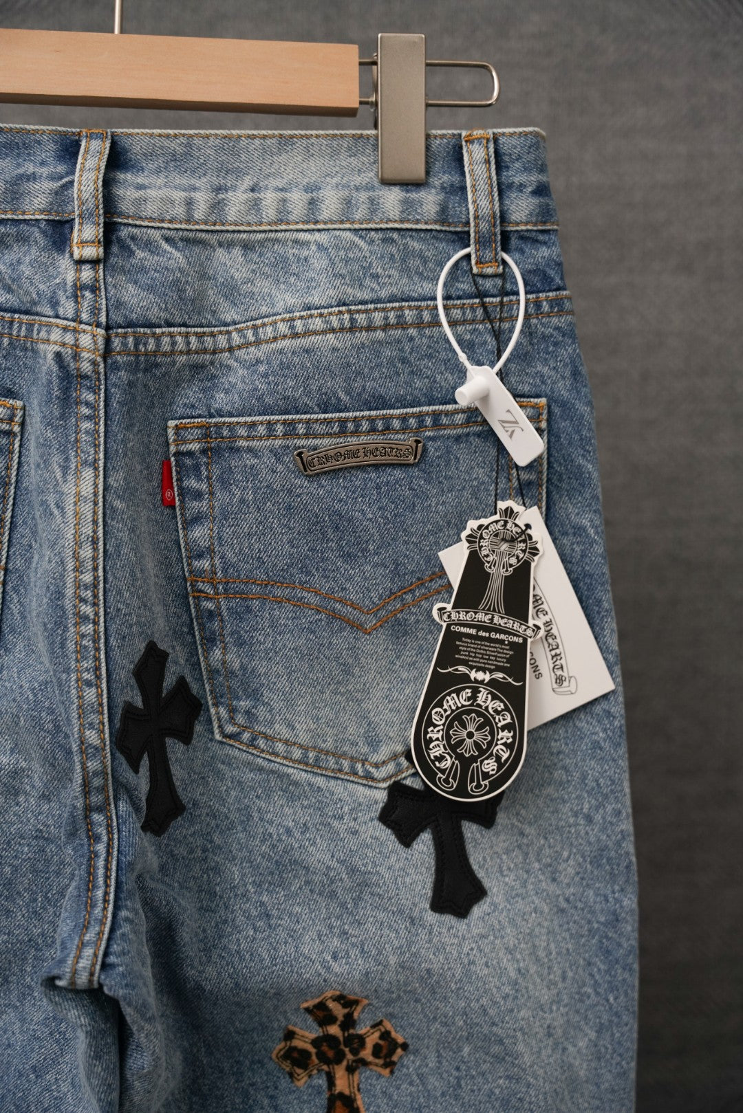 Blue denim pants with cross patches and hanging hangtag on back pocket