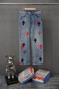 Light blue denim pants with scattered cross patches, front view on hanger